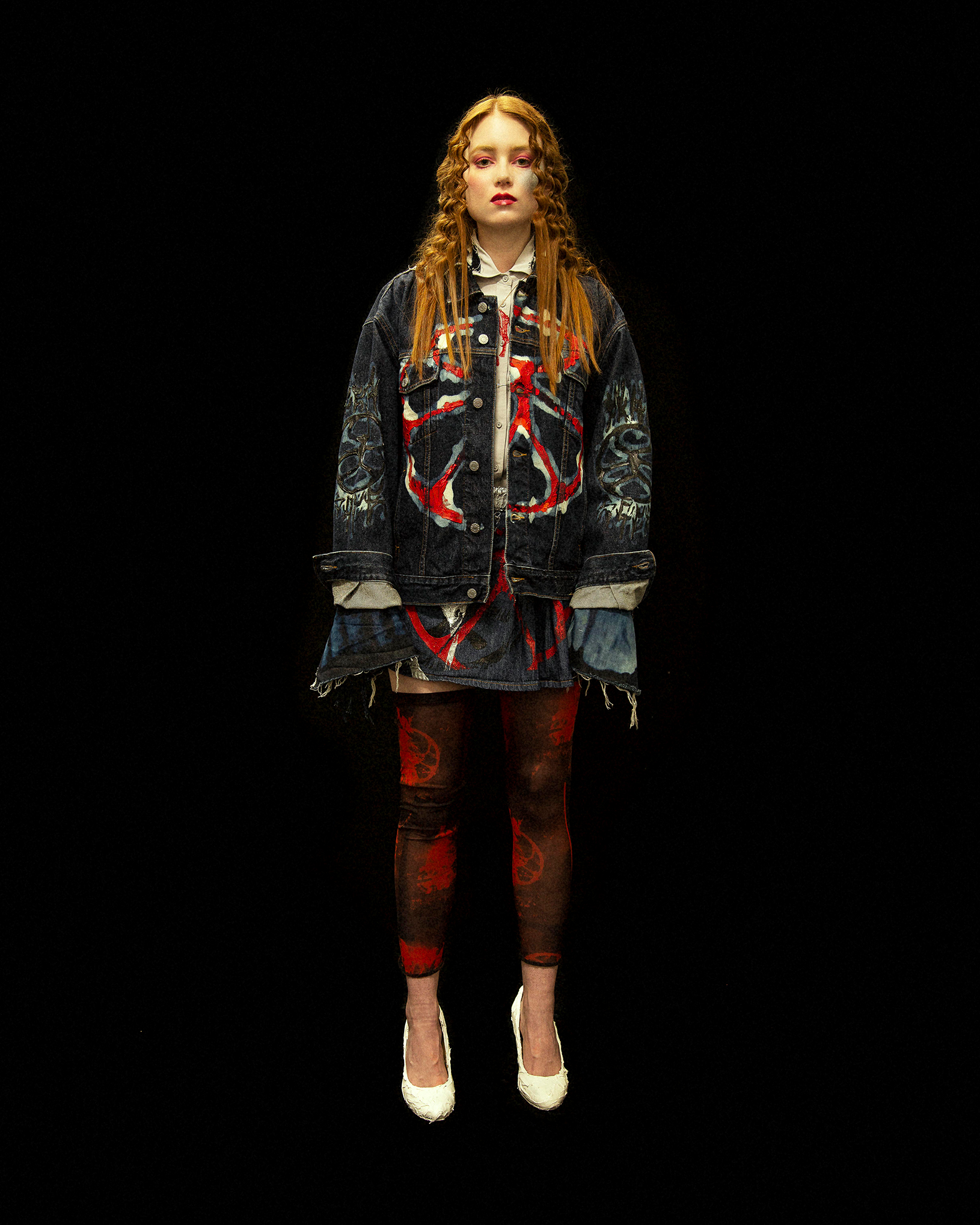 Full body image of a model facing the camera against a black background wearing a patchwork denim jacket and dark red leggings